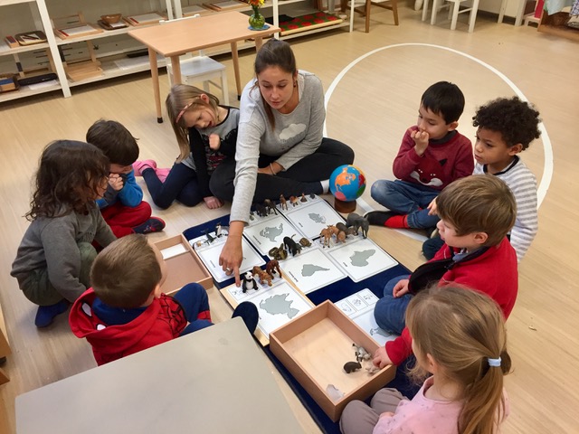 L'éducatrice Montessori 3 - 6 ans fait une présentation sur les continents et les animaux à un groupe d'enfants assis autour d'elle.
