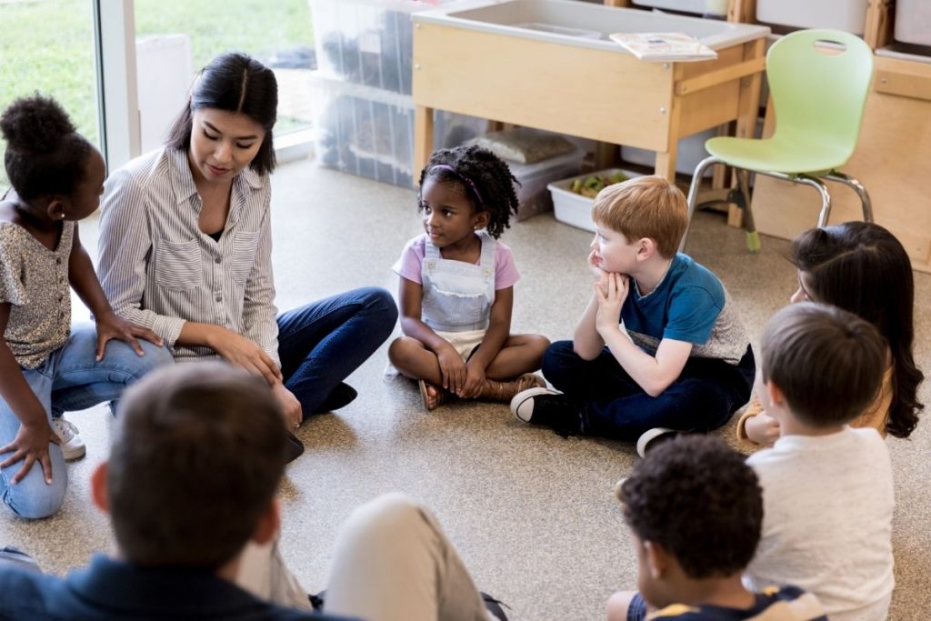 Les enfants se regroupent pour une activité de groupe avec leur enseignante à l'école. La leçon de silence Montessori.